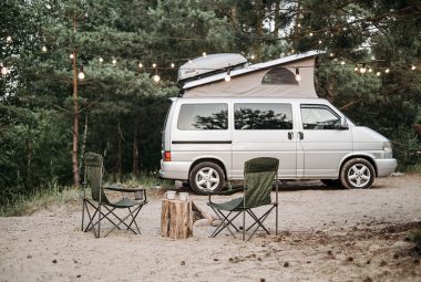 Class B RV Camper Van at a sandy campsite with chairs and a string of lights
