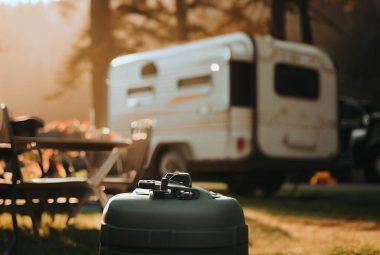portable rv waste tank in focus with RV and campsite in a blurred background