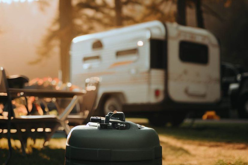 portable rv waste tank in focus with RV and campsite in a blurred background